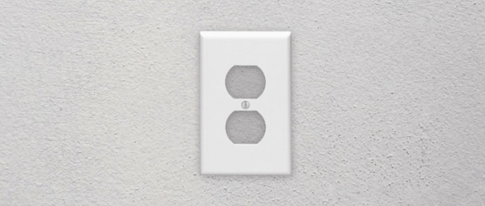 A white Leviton Duplex Device Receptacle Wallplate on a grey wall inside a home.