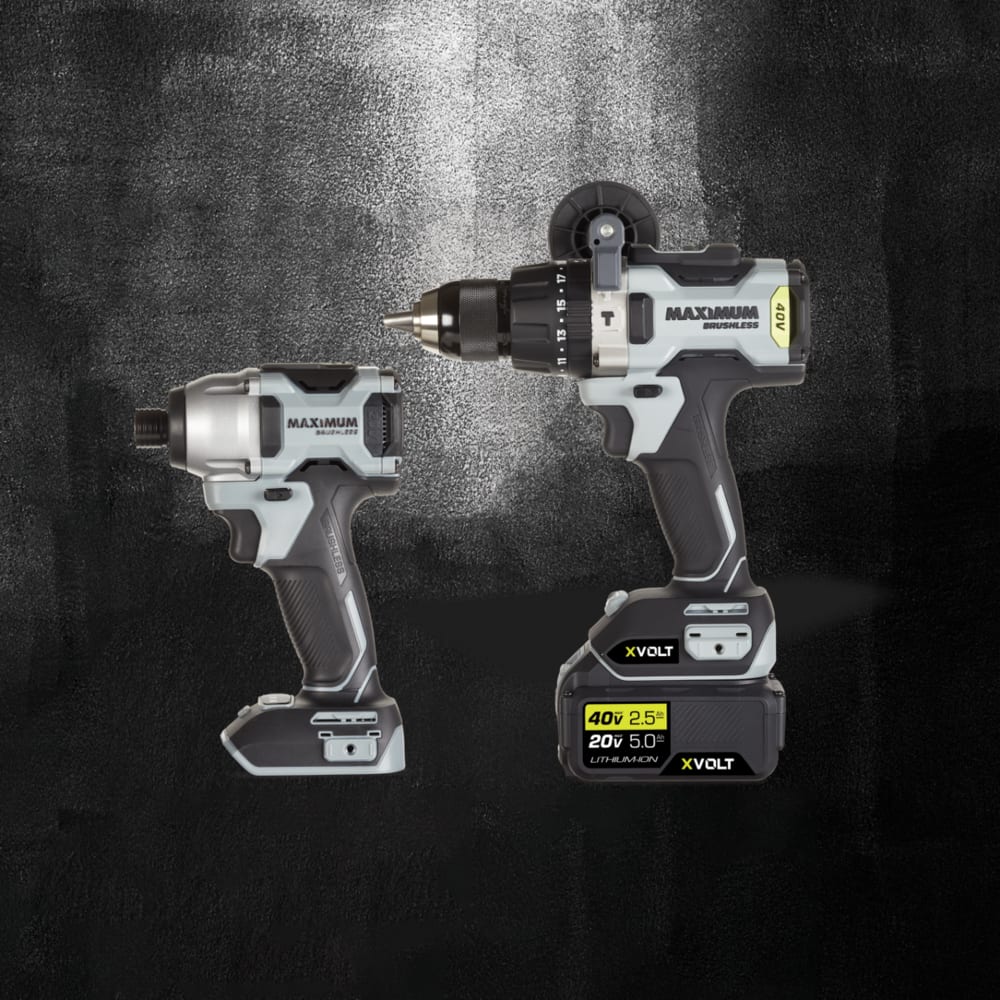 A hammer drill/driver and impact driver pictured together set against a dark grey and black background. 