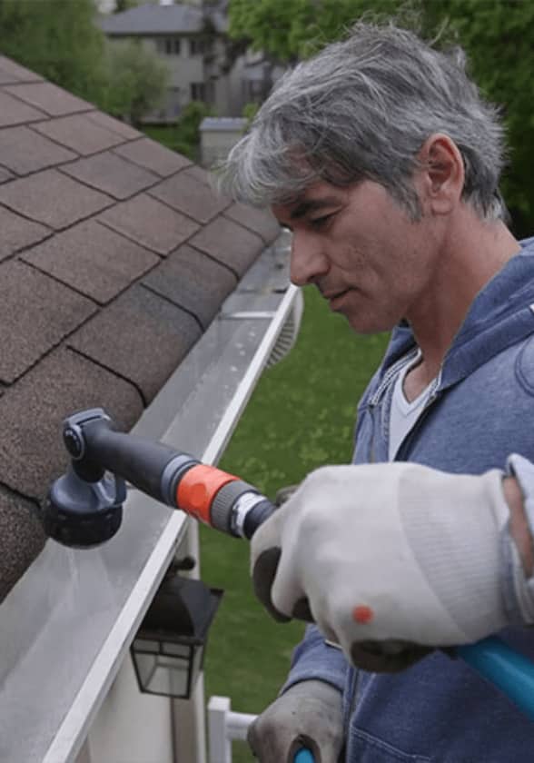 A man uses a hose to clean out roof gutters.