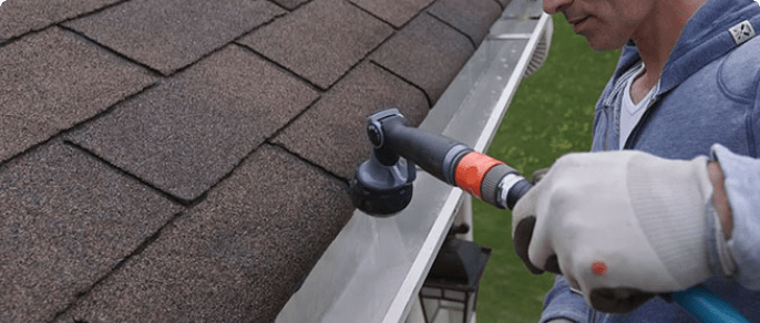 A man uses a hose to clean out roof gutters.