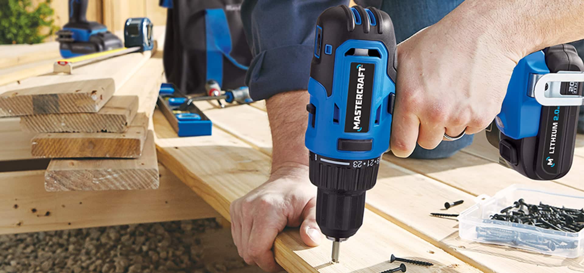 Hand using a blue cordless Mastercraft drill to drill holes in wood.