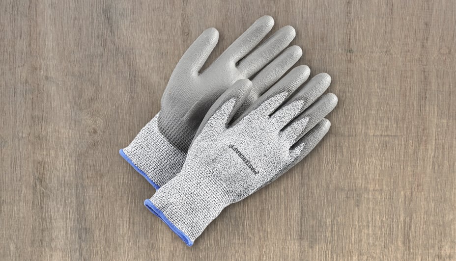 Close-up of black-and-grey work gloves held in the hand of a worker in blue coveralls.