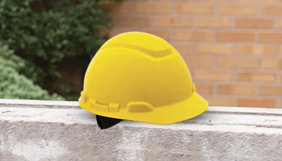A yellow plastic hard hat rests on a concrete step, set against a brick background.