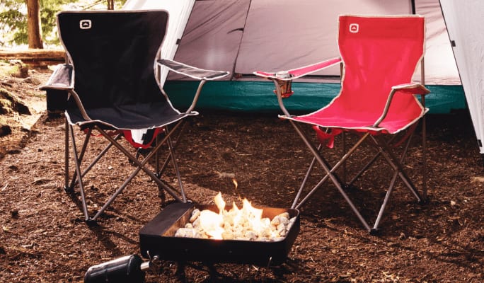 Black camping chair and red camping chair in front of a tent at a campsite.