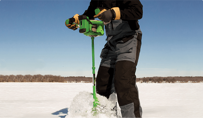 Person using an ice auger drill on a frozen lake. 