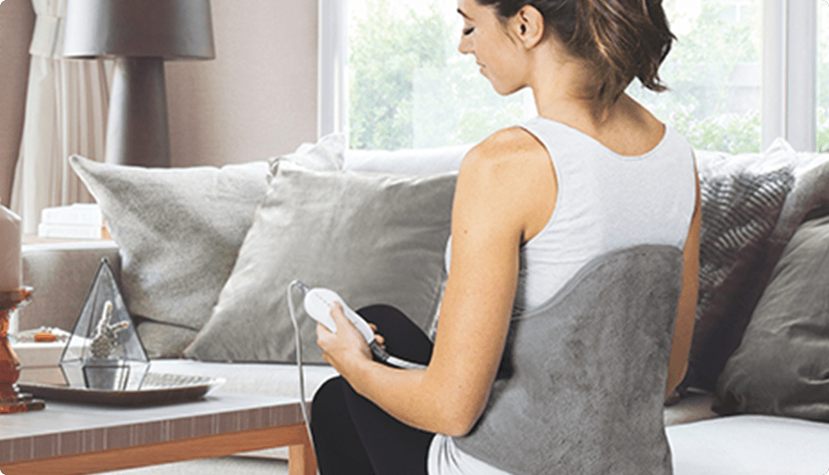 Woman uses a portable back massager wrap in a living room.
