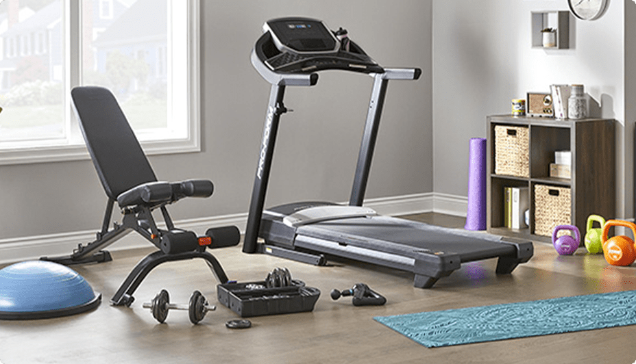 Home gym with treadmill, Bowflex stowable bench, cap barbell dumbbell weights set, Theragun prime massager, balance trainer, kettle bells, and yoga mats.