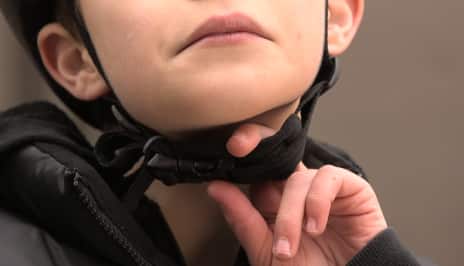 Boy checking helmet strap under the chin with one finger.