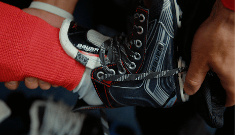 Une image en gros plan d’une main adulte plaçant un patin de hockey noir sur le pied d’un enfant.