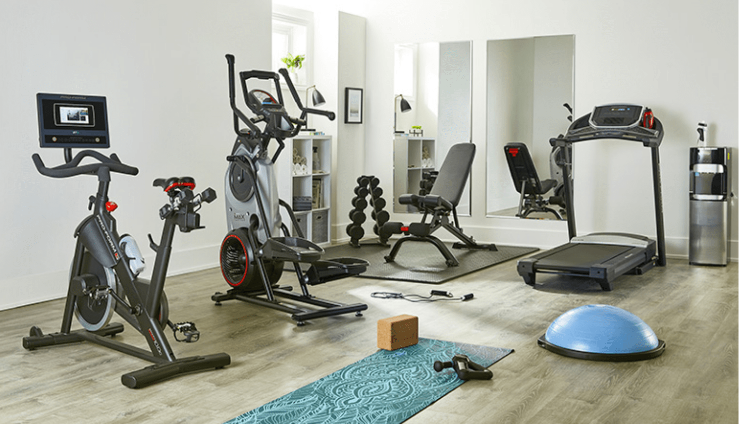 Exerciseur elliptique, banc de musculation, vélo stationnaire et poids dans un coin spacieux