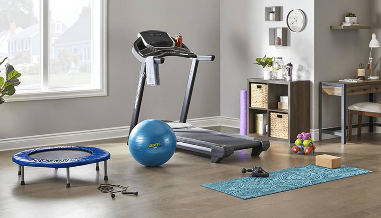 Yoga mat, treadmill, exercise ball and weights near a window.
