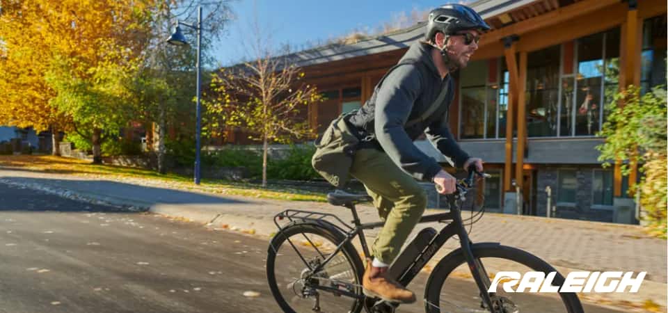 A man rides a Raleigh bike along a sunny residential street.