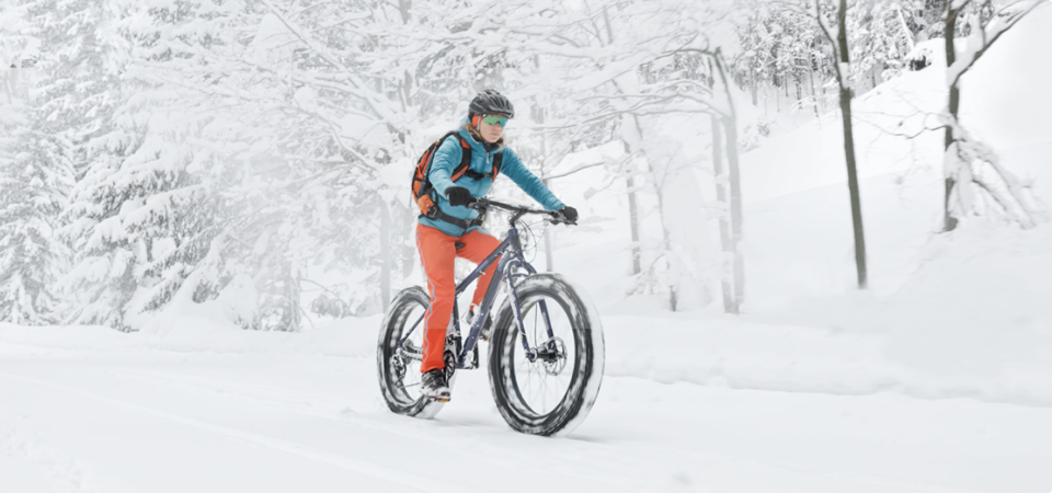 Une personne à vélo dans la neige avec une tenue de cycliste d'hiver.