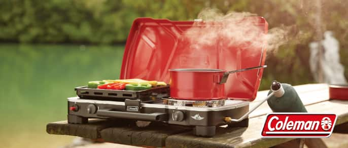 Red Coleman burner stove with pot and vegetables.