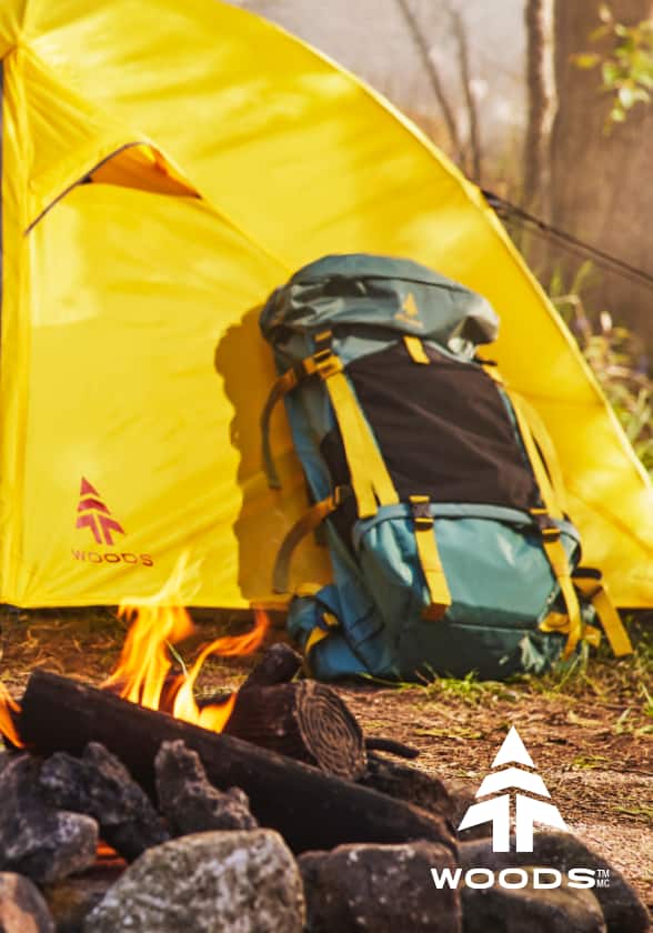 Yellow Woods camping tent and green backpack behind a campfire.
