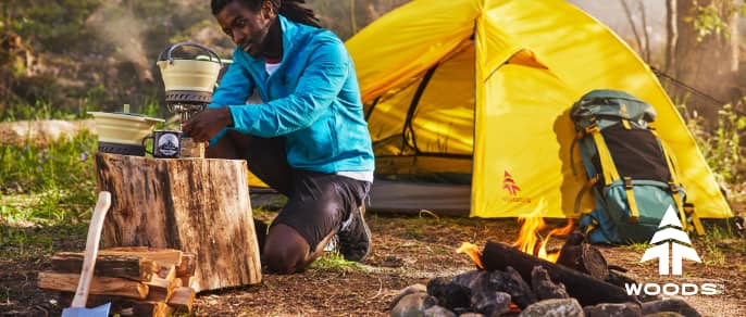 Yellow Woods camping tent and green backpack behind a campfire.