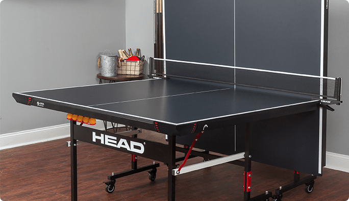 A black HEAD Summit Table Tennis Table with one half folded vertically against a wall inside a home.