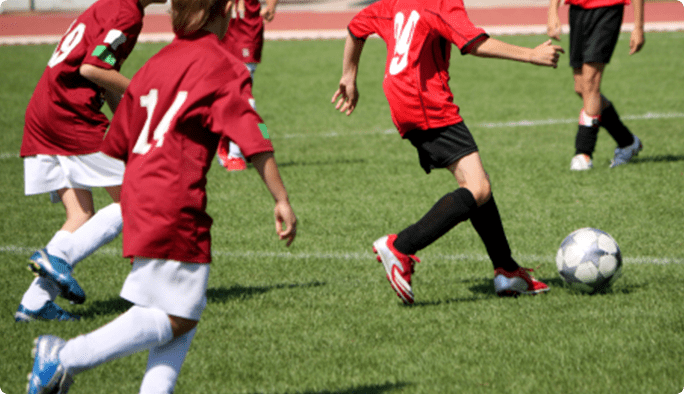 Soccer players in red jerseys pursue a soccer ball on a green pitch.