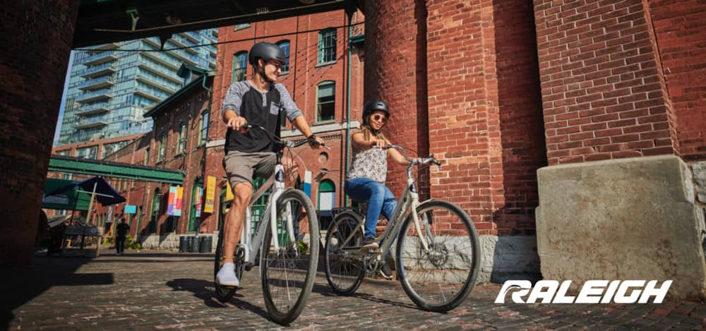 A man rides a Raleigh bike along a sunny residential street.