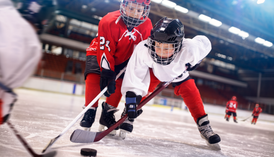 Un joueur de hockey adolescent en chandail d’entraînement rouge qui regarde un adolescent dans un chandail d’entraînement blanc à l’intérieur d’une patinoire de hockey.