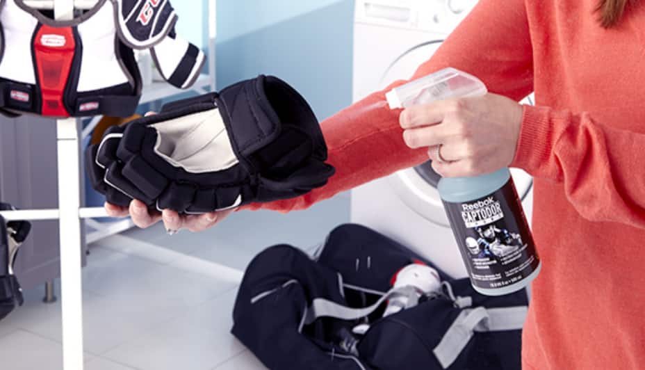 A person sprays disinfectant into a black hockey glove.