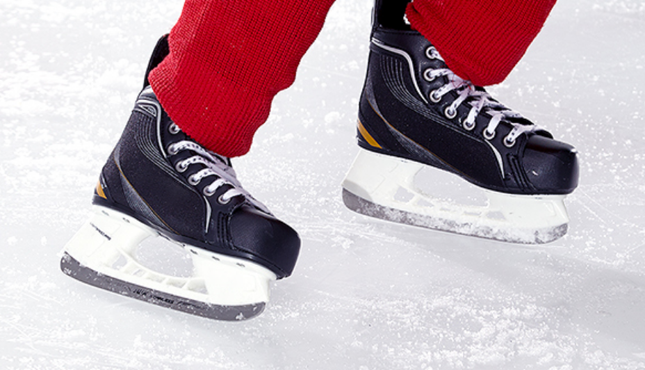 A closeup image of hockey player’s skates as they skate on the ice.