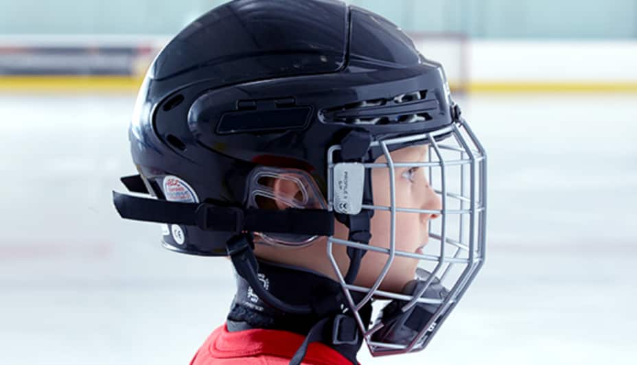 A child wears a black hockey helmet and wire cage mask in a hockey rink.