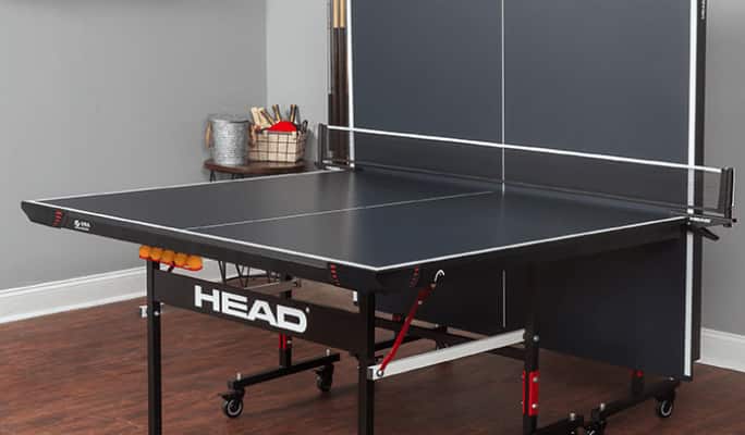 Black HEAD Summit Table Tennis Table with one half folded vertically against a wall inside a home.