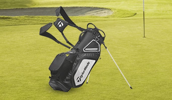Un sac de golf à support TaylorMade 8.0 noir reposant à côté d'un trou sur un terrain de golf verdoyant.