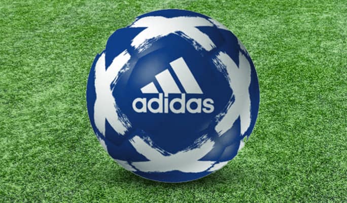 A blue adidas Starlancer V soccer ball with a white X pattern rests on a green soccer pitch.