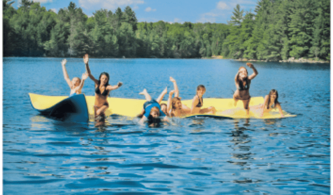 Group of people on a yellow floating water mat on a lake.