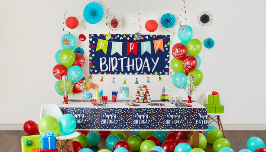 Table d’anniversaire avec bannière « Happy Birthday » sur le mur, entourée de cadeaux, de décorations de fête et de ballons 