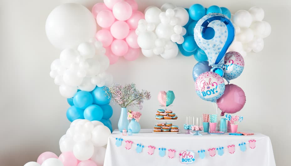 Présentoir de ballons blancs, roses et bleus derrière une table blanche avec décorations de table assorties. 