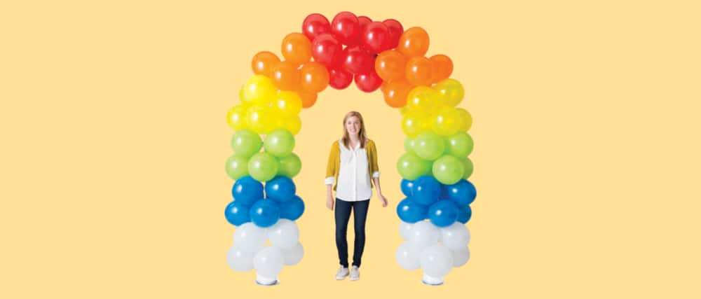 Woman standing under a white, blue green, orange and red balloon arch. 
