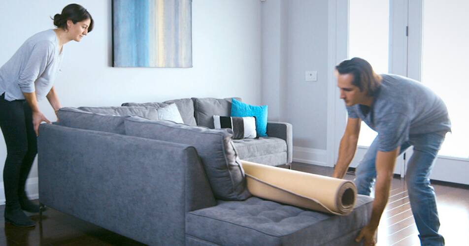 A couple moving their sofa to the middle of the room.