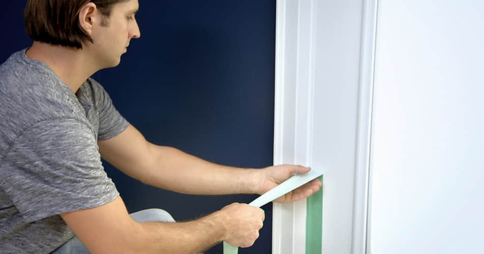 A man applying tape next to the trim of a door. 