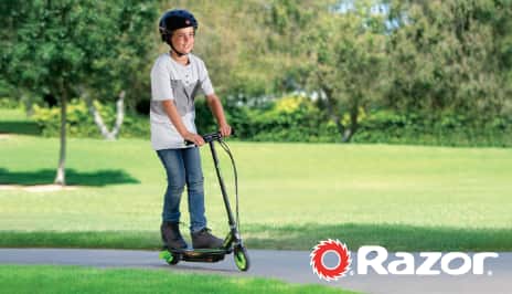 A boy riding a Razor scooter in a park.