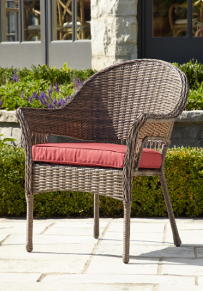 A brown wicker patio armchair with a read cushion placed on it sitting in sunlight. 
