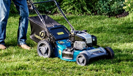 Person pushing a blue lawnmower across grass. 