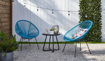 Ensemble à 3 pièces Acapulco avec 2 chaises bleues, coussin multicolore et table basse en verre avec bougie, plante verte et verre.