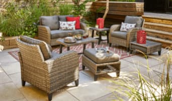 Breton wicker patio loveseat, armchairs, ottoman and coffee tables on a rug.