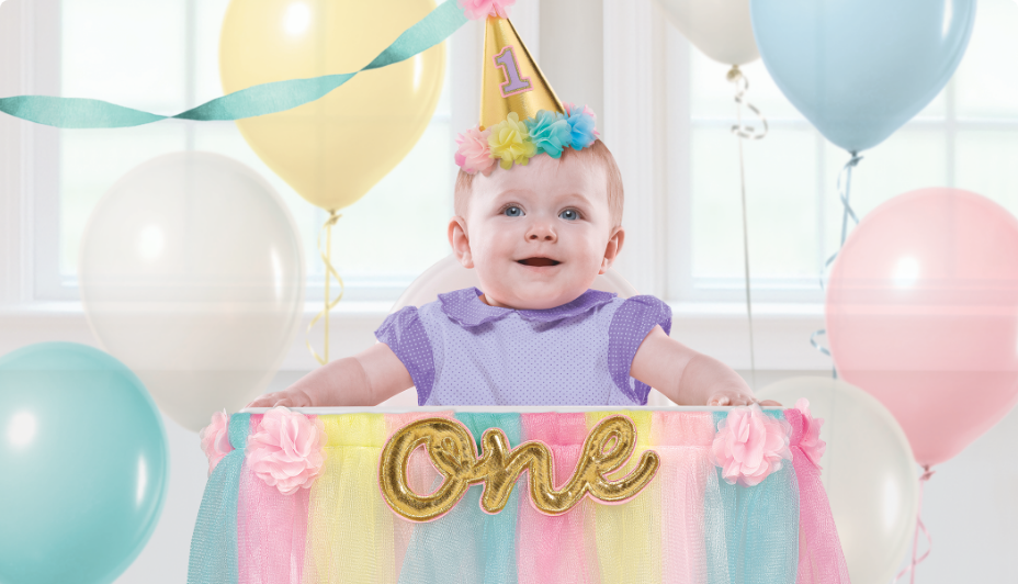 Baby wearing a party hat with balloons in the background.