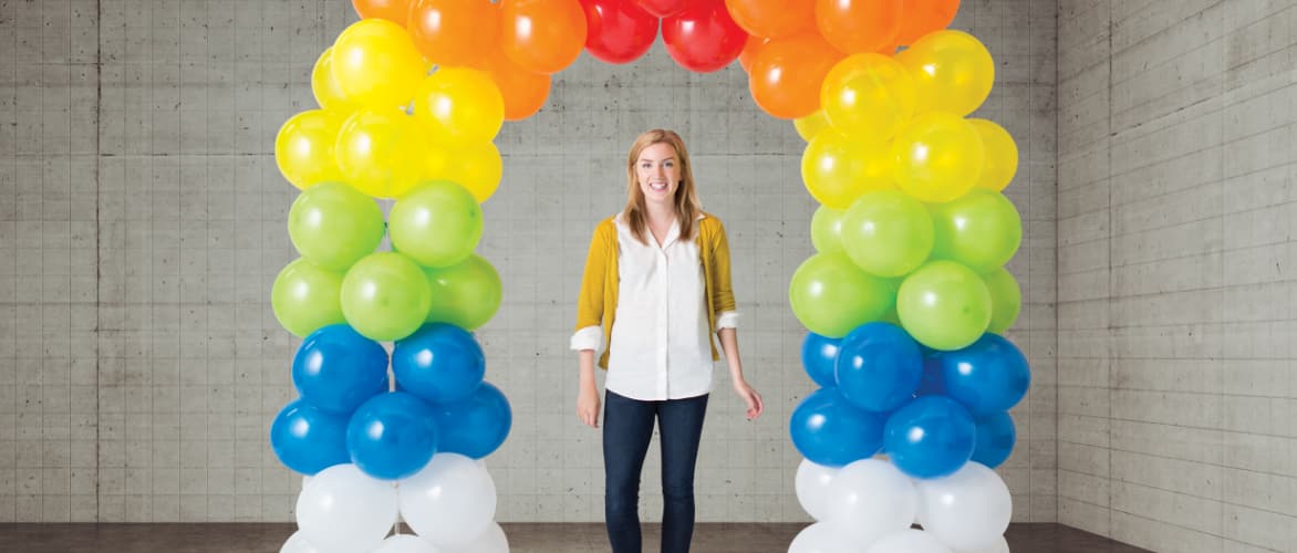 Une femme se tenant sous une arche de ballons multicolore.