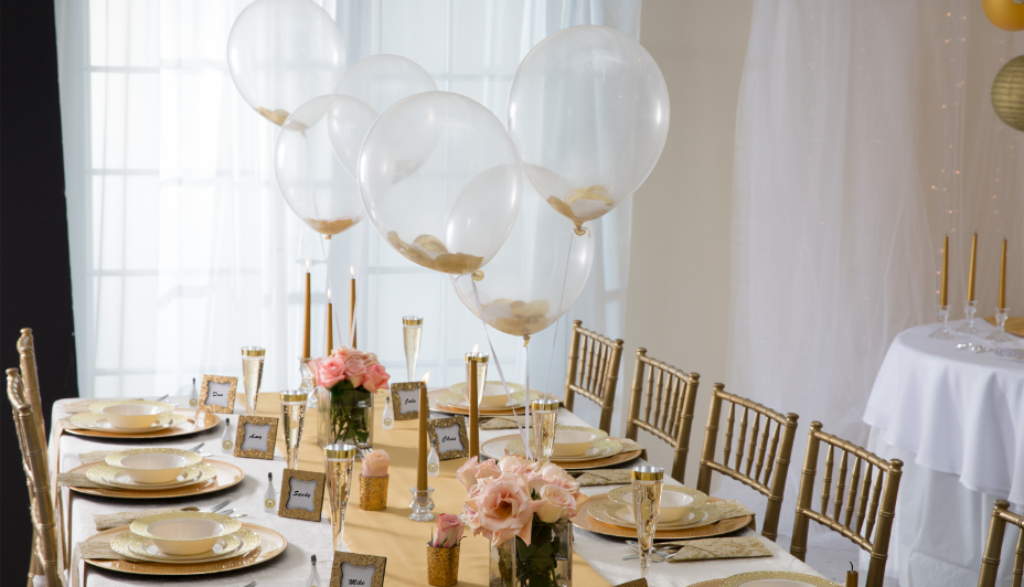 Elegant gold and white table setting with matching gold décor and clear floating balloons. 