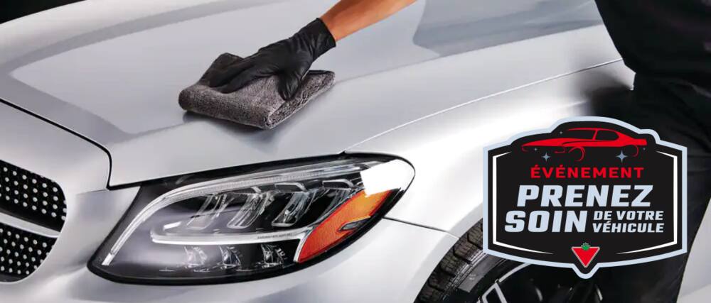 A gloved hand wiping the hood of a silver automobile with a microfibre cloth.