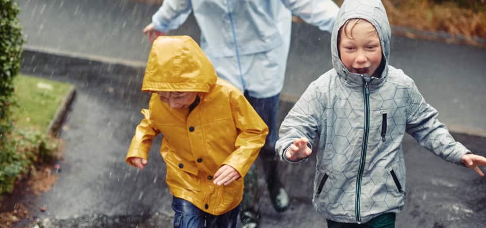 Two kids wearing raincoats running outside in rainy weather