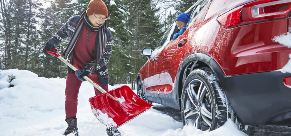 Une personne pelletant de la neige à côté de sa voiture