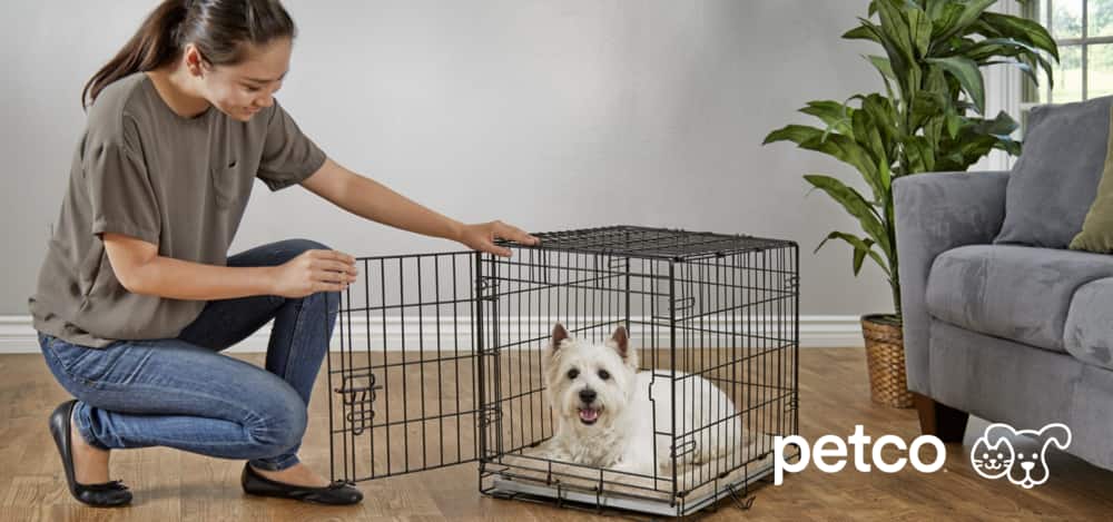 Woman beside Petco dog cage with white dog inside
