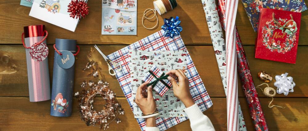 Une personne emballant des cadeaux de Noël avec du papier d’emballage et des nœuds