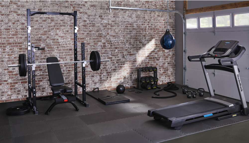 A weightlifting rack, full dumbell rack, punching bag, treadmill, and assorted accessories in a garage.